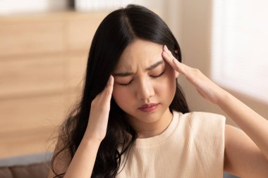 Asyalı genç kadının migreni var ve evdeki rahat yatak odasında uyandıktan sonra baş ağrısı, aniden ağrı kesicilerin etrafındaki baş masajına acı dolu bir saldırı, sağlık konsepti.