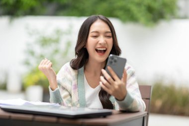 Milenyum Asyalı genç bir kadın cep telefonuna bakıyor. İyi haberlerle gülüyor ya da internetten alışveriş yapıyor. Cep telefonu uygulamasına bakan mutlu ve neşeli bir kadın heyecanlı hissediyor.
