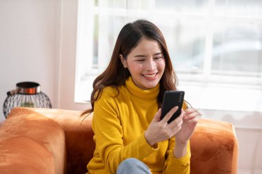 Mutluluk Girişimcisi güzel iş kadını Asyalı genç kadın online alışveriş için günlük kullanım cep telefonu takıyor. Ev ortamında sosyal medya ve dizüstü bilgisayarla iyi eğlenceler. İnternet bankacılığı.