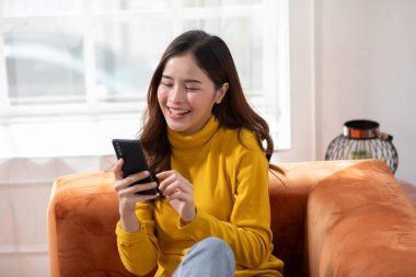 Mutluluk Girişimcisi güzel iş kadını Asyalı genç kadın online alışveriş için günlük kullanım cep telefonu takıyor. Ev ortamında sosyal medya ve dizüstü bilgisayarla iyi eğlenceler. İnternet bankacılığı.