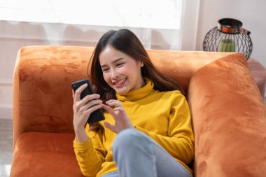 Mutluluk Girişimcisi güzel iş kadını Asyalı genç kadın online alışveriş için günlük kullanım cep telefonu takıyor. Ev ortamında sosyal medya ve dizüstü bilgisayarla iyi eğlenceler. İnternet bankacılığı.