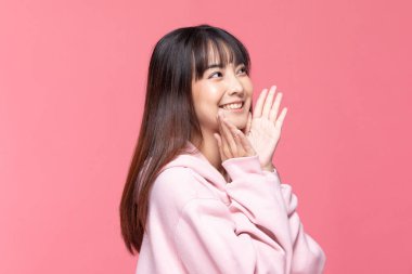 Genç ve güzel Asyalı kadın gülümsüyor. Temiz ve taze tenli. Mutluluk ve neşe dolu. Pozitif duygusal olarak yukarıyı işaret eden, pembe arka planda izole edilmiş.