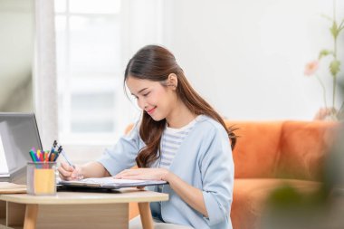 Güzel Asyalı genç bir kadın bilgisayar dizüstü bilgisayarı kullanarak kanepeye oturur sosyal medyada rahatlar, gülümser ve güler. Çevrimiçi satış pazarlamasında çalışan serbest çalışan bir kadın. İnternetten alışveriş.