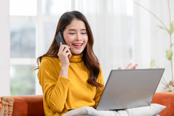 Asian Woman Multitasks Seamlessly Working Laptop While Engaging Professional Phone Stock Photo