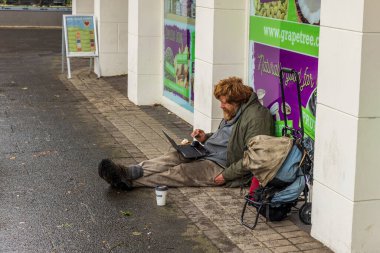 Evsiz biri dizüstü bilgisayarla yerde oturuyordu.