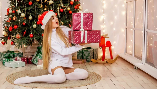 선물을 소녀는 크리스마스 근처에 있습니다 산타클로스 모자를 스웨터를 소녀는 카메라를 — 스톡 사진