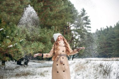 Çam ormanındaki bir kız elleriyle kar atıyor ve seviniyor. Yeni yıl, Noel, kartpostal, pankart. Metin için yer.