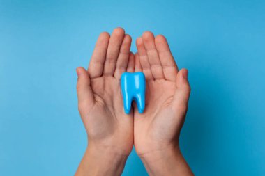 Mavi arka planda büyük bir dişi tutan bir el. Diş bakımı kavramı. Diş Temizliği ve Ağız Sağlığı. Yakın plan. Metin için yer.