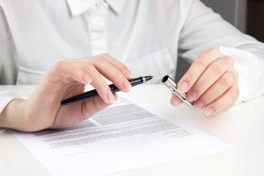 A young woman in a white blouse removes the cap from a pen to start filling out bills, resumes, documents