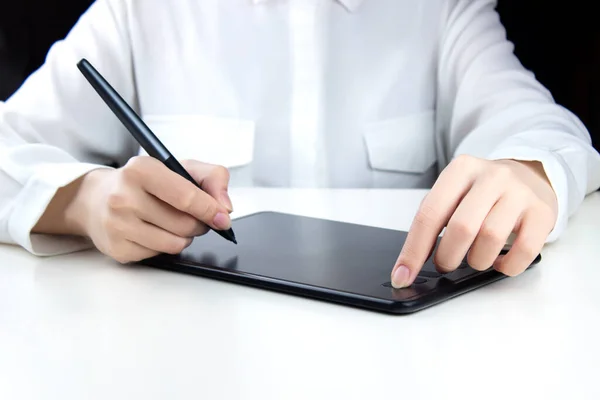 A young girl works on a wireless graphics tablet, holds a pen in one hand, and presses a button with the other