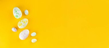 Farklı renklerde renkli tavuk ve bıldırcın yumurtaları sarı arka planda yatar. Üst görünüm, bir sürü boşluk