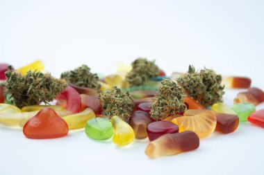 Kurumuş tıbbi marihuana tomurcukları çeşitli şekillerde ve tatlarda sakızların arasında yatar. Soğuk beyaz bir arka planda