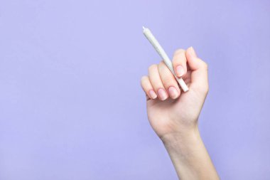 Doğal tırnakları olan bir kadının elinde açık mor bir arka planda tıbbi marihuana ile esrar bulunur. Boşluğu kopyala