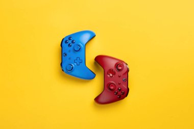 İki tane Xbox marka kablosuz oyun pedi sarı arka planda sırt sırta yatar. Takım oyunu, çok yer var.