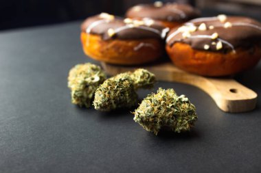 Arka planda çikolata kremalı, fındık kırıntılarıyla serpiştirilmiş kuru tıbbi marihuana tomurcukları var. Siyah bir arkaplanda
