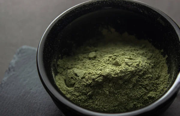 stock image Green powder in a small ceramic bowl, on a stone stand, on a black background.  Super food or marijuana kief concept