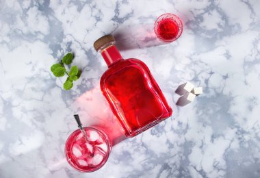 Bir şişe kırmızı alkol, bir bardak likör ve buzlu kokteyl ile eski moda bir bardak ve yeniden kullanılabilir bir pipet. Yanında bir tutam nane ve absent için üç parça şeker. Mermer bir sırt deliğinde