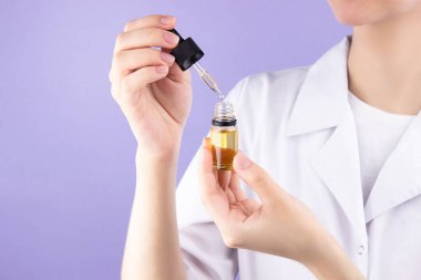 Bir doktorun elinde, içinde cbd yağı özü olan bir pipetle birlikte bir cam şişe, avucunun içinde, kurumuş bir tıbbi marihuana tomurcuğu. Tıbbi kenevirle alternatif tedavi. Doktorun göğsünde kanserle mücadele işareti var.