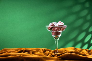 Kırmızı plastik poker çipleri, kahverengi kadife kumaşın üzerindeki cam margarita bardağında yatıyor. Bardağın kenarındaki küçük iskambil kağıtlarının hayranı. Kokteyl dekorasyonu gibi. Yan görünüm