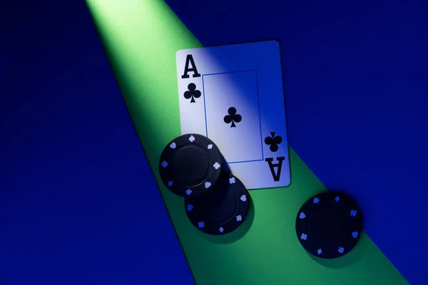 A plastic playing card lies on a blue-green background, next to three chips.