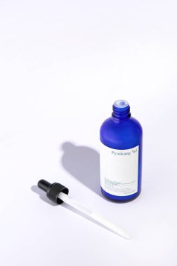 Açık cam bir şişe Pyunkang Yul marka nemlendirici serum. Beyaz bir arka planda duruyor, bir pipetin yanında..