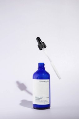 Açık cam bir şişe Pyunkang Yul marka nemlendirici serum. Beyaz bir arka planda duruyor, bir pipet yakınlarda uçuyor.