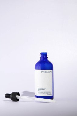 Açık cam bir şişe Pyunkang Yul marka nemlendirici serum. Beyaz bir arka planda duruyor, bir pipetin yanında..