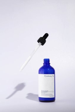 Açık cam bir şişe Pyunkang Yul marka nemlendirici serum. Beyaz bir arka planda duruyor, bir pipet yakınlarda uçuyor.