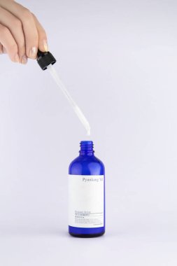 Bir kadının eli, Pyunkang Yul marka nemlendirici serumun açık cam şişesine pipet düşürür. Beyaz bir arkaplanda