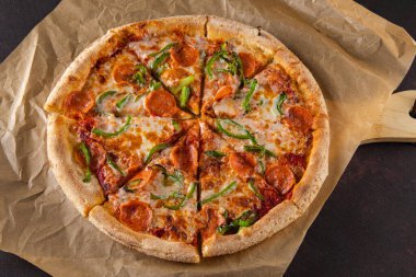 İnce hamurlu güzel renkli biberli pizza. Sosisli ve biberli. Siyah arkaplanda parşömenin üzerinde.