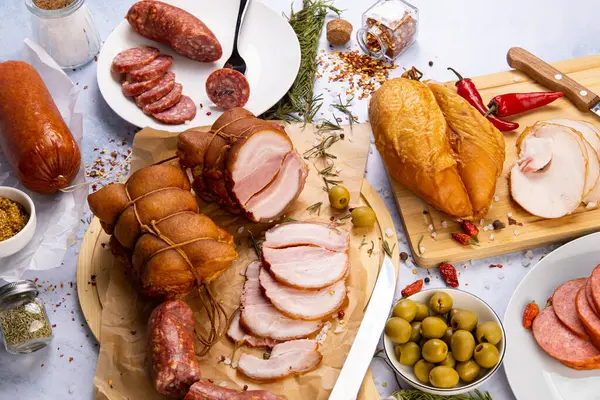 an abundance of meat delicacies on a concrete background surrounded by various spices and herbs, olives, peppers