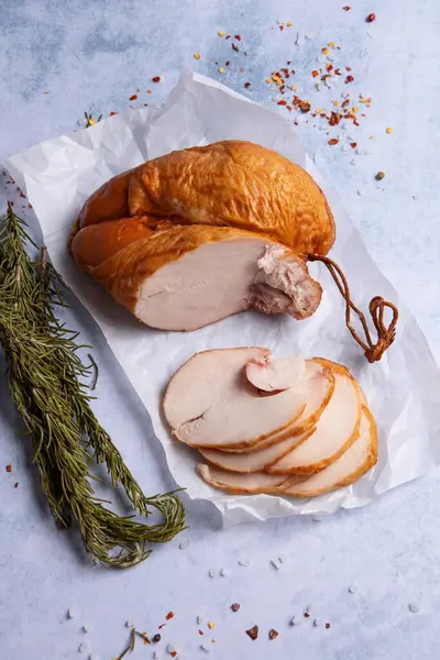 deli meat - smoked chicken breast sliced on white parchment surrounded by herbs and spices