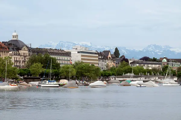 stock image Boats and yachts parked at the shore with neo-classical and modern buildings and distant snowy mountain peaks in the background