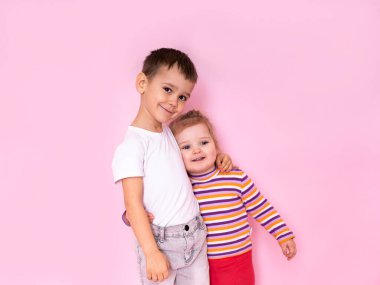 cute kids hugging on a pink background. Brother and sister look at the camera.