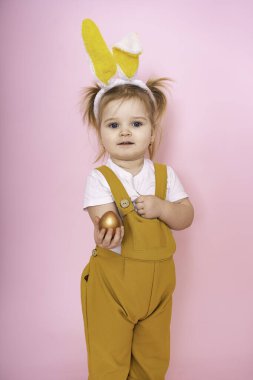 Kafasında tavşan kulakları olan neşeli bir kız pembe arka planda boyanmış bir yumurta gösteriyor. Komik, delicesine mutlu bir çocuk. Bir çocuk için Paskalya