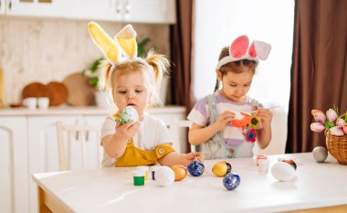 İki mutlu çocuk, kar beyazı bir mutfakta Paskalya yumurtası çiziyor. Bir kız Paskalya yumurtası gösterir. Mutluluk kavramı, çocuklar için Paskalya tatili.