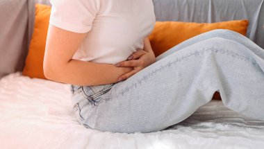 Evdeki kanepede otururken şiddetli karın ağrısı çeken genç bir kadın. Yakın plan..