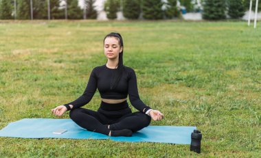 Açık hava parkında spor kıyafetli beyaz bir kadının spor minderde rahatlamış bir portresi. Sağlıklı aktif yaşam biçimi.