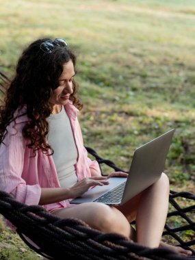 Woman working remotely in hammock with laptop clipart