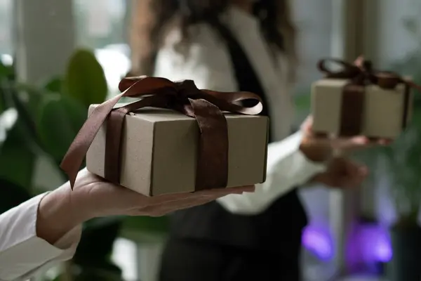 Kahverengi kurdeleyle süslenmiş bir hediye sunan eller..