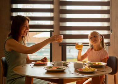 Anne ve kızı kahvaltı masasında portakal suyu içiyor..