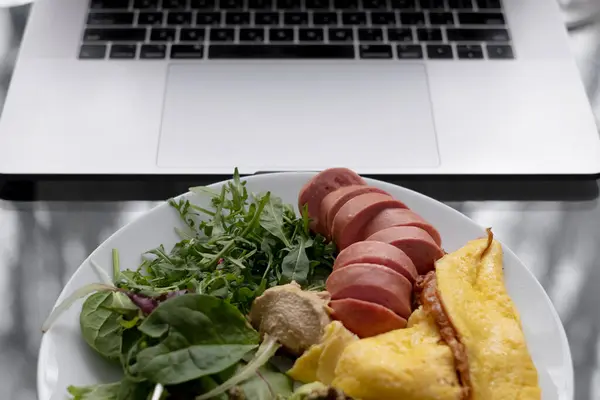 Laptopun yanında sebzeli omlet ve sosisli sağlıklı besleyici kahvaltı.