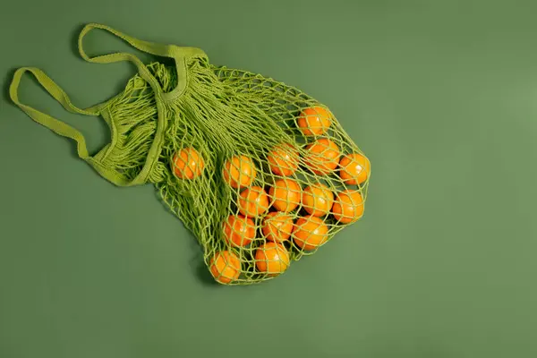 Mandarinler bir ağ torbasında, canlı yeşil bir arkaplanda.