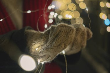 Ellerinde parlak çelenkler, Noel ışıkları, bokeh etkisi, bayram süslemeleri, kış sıcaklığı.