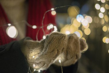Ellerinde parlak çelenkler, Noel ışıkları, bokeh etkisi, bayram süslemeleri, kış sıcaklığı.