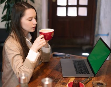 Laptop kullanan ve kafe masasında kahve içen bir kadın.