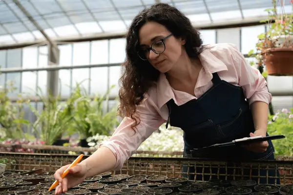 Kadın fideleri kontrol ediyor ve serada sonuç yazıyor.