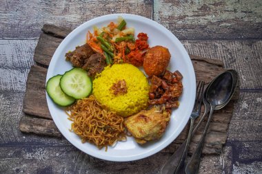 Indonesian traditional food, nasi kuning / yellow turmeric rice served with beef rendang, fried chicken, vegetables, spicy eggs, noodles, and tempeh
