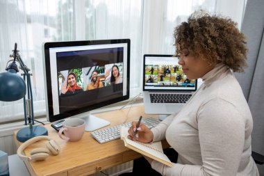 Woman making notes during video conference at home