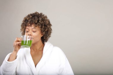 Bornozlu, yeşil çay içen bir kadının stüdyo fotoğrafı.